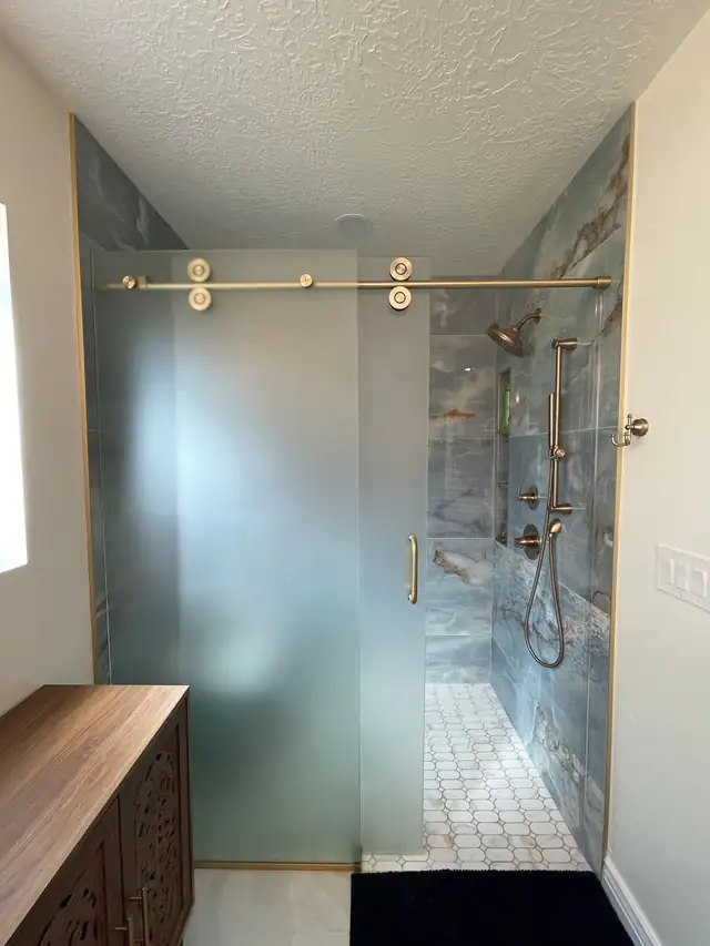 Walk-in shower with frosted glass sliding door on a brass rail, blue stone-look wall tile and brass shower set