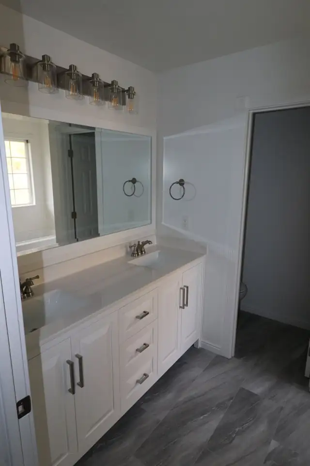 White vanity with light countertop, large mirror and towel ring