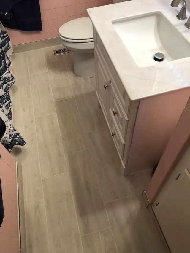 White vanity with marble-look top and wood-look plank floor in a bathroom with pink wall tile